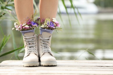 Woman standing on wooden pier with flowers in socks outdoors, closeup. Space for text