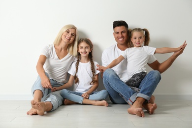 Happy family sitting on floor near white wall