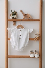 Baby bodysuit, shoes, toys and small bouquet on ladder near white wall
