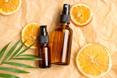 Bottles of organic cosmetic products, dried orange slices and green leaf on parchment paper, flat lay