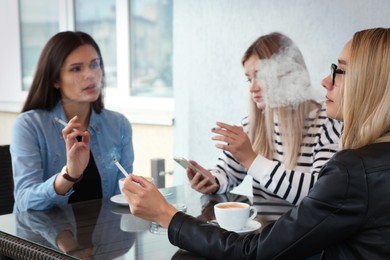 Photo of Women smoking cigarette at table in outdoor cafe