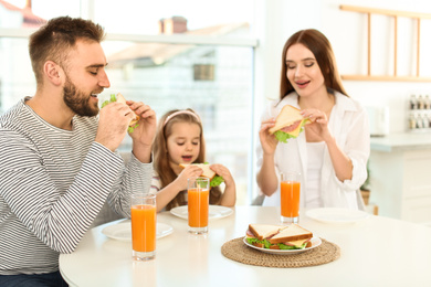 Happy family having breakfast with sandwiches at table in kitchen