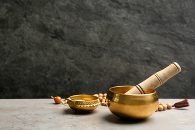 Golden singing bowl with mallet on grey table against dark background, space for text. Sound healing
