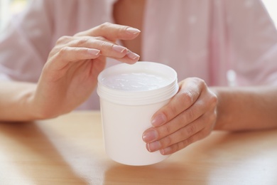 Woman with jar of moisturizing cream at table, closeup
