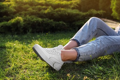 Woman in jeans and white shoes relaxing on green grass, closeup. Space for text