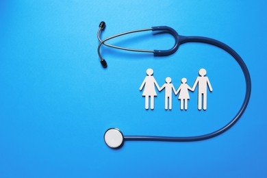 Photo of Figures of family near stethoscope on light blue background, flat lay. Space for text. Insurance concept