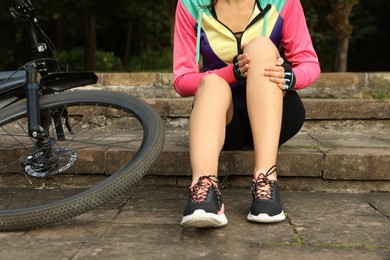 Woman with injured knee on steps near bicycle outdoors, closeup