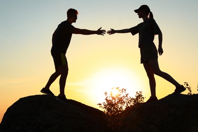 Photo of Hiker helping friend outdoors at sunset. Help and support concept