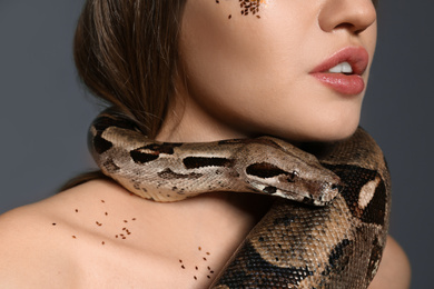 Photo of Young woman with boa constrictor on grey background, closeup