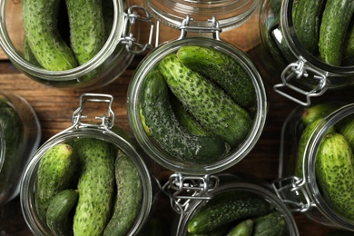 Pickling jars with fresh cucumbers on wooden table, flat lay