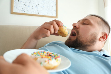 Lazy overweight man eating donuts at home, closeup