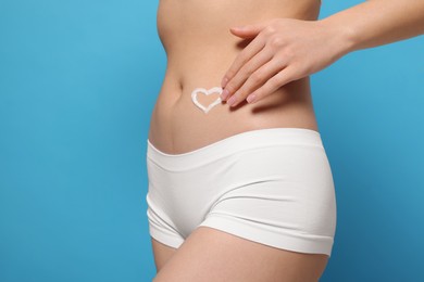 Photo of Woman with heart made of body cream on her belly against light blue background, closeup. Space for text