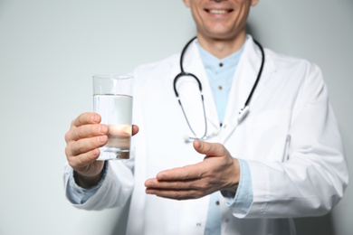 Nutritionist holding glass of pure water on light grey background, focus on hand