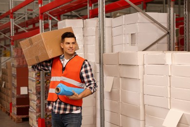 Worker with roll of stretch film and wrapped box in warehouse
