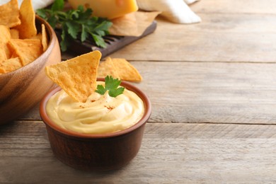 Photo of Delicious cheese sauce with nacho and parsley on wooden table, space for text