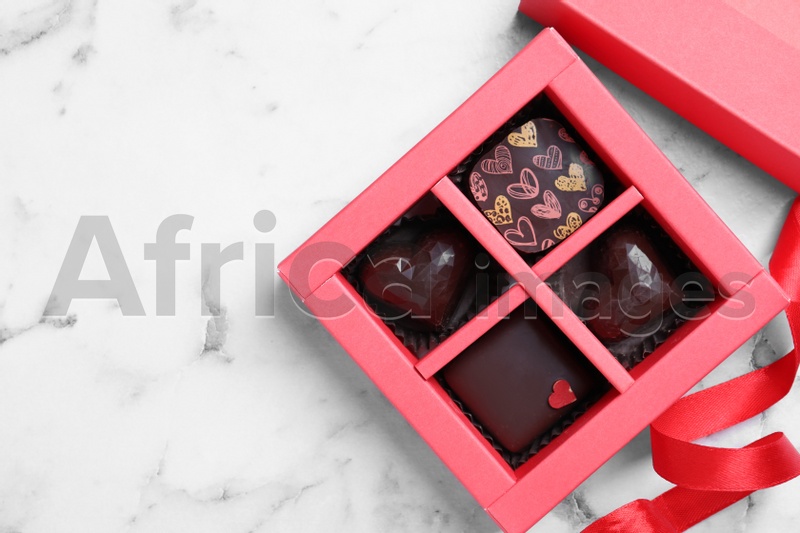Photo of Box with tasty chocolate candies on white marble table, flat lay