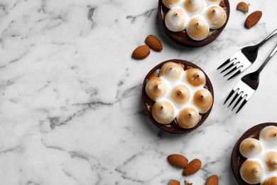 Delicious salted caramel chocolate tarts with meringue and almonds on white marble table, flat lay. Space for text