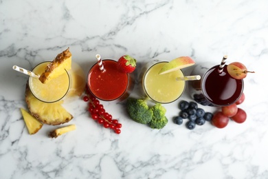 Photo of Glasses of delicious juices and fresh ingredients on white marble table, flat lay
