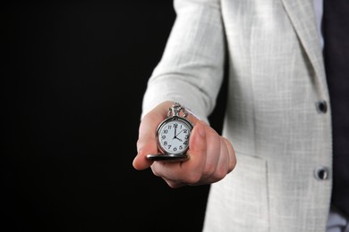 Closeup view of businessman holding pocket watch on black background, space for text. Time management