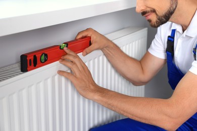 Photo of Professional plumber using bubble level for installing new heating radiator indoors, closeup