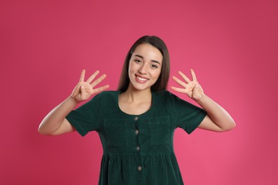 Woman showing number eight with her hands on pink background
