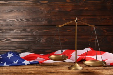 Scales of justice and American flag on wooden table. Space for text