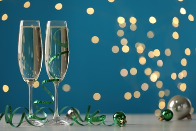 Glasses of champagne with serpentine streamers and Christmas balls on table against blurred lights. Space for text