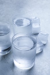 Shot glasses of vodka with ice on light grey table