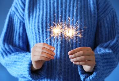 Woman holding burning sparklers on blue background, closeup