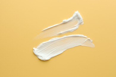 Samples of face cream on yellow background, top view