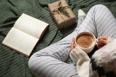 Woman in knitted socks sitting on warm plaid with hot cocoa, closeup
