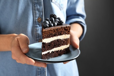Woman holding plate with slice of chocolate sponge berry cake on grey background, closeup