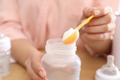 Woman preparing infant formula at table, closeup. Baby milk