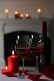 Photo of Glasses of red wine, burning candles and rose flowers on grey table indoors. Romantic atmosphere