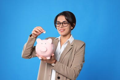 Photo of Young woman putting coin into piggy bank on light blue background