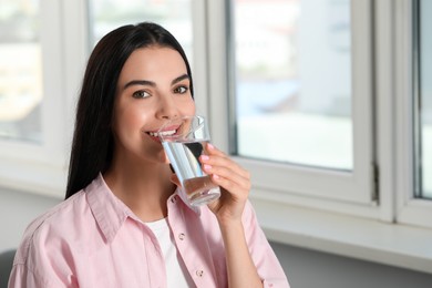 Young woman drinking water indoors, space for text. Refreshing drink