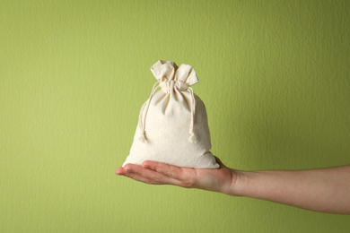 Woman holding full cotton eco bag on light green background, closeup