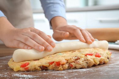 Woman putting marzipan into raw dough for Stollen at wooden table, closeup. Baking traditional German Christmas bread