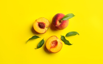 Fresh ripe peaches and green leaves on yellow background, flat lay