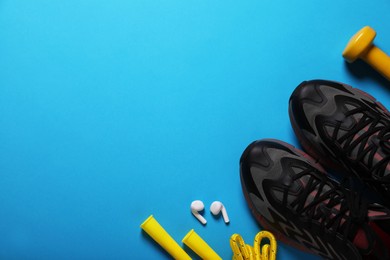 Sneakers, skipping rope and dumbbell on light blue background, flat lay with space for text. Morning exercise