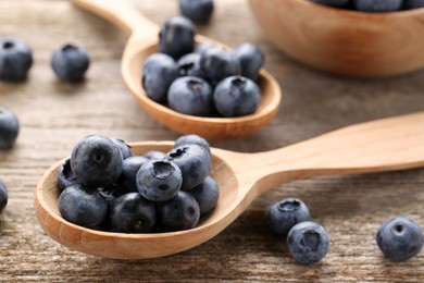 Spoons with tasty fresh blueberries on wooden table, closeup