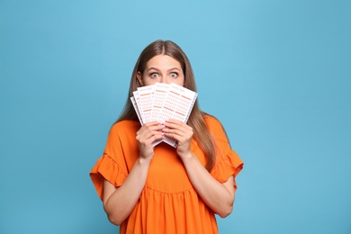 Portrait of emotional young woman with lottery tickets on light blue background