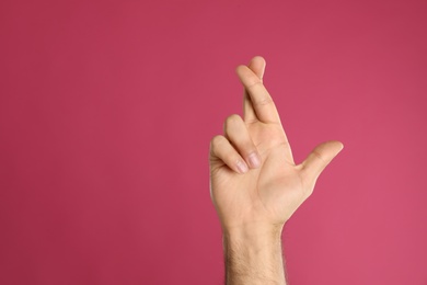 Man with crossed fingers and space for text on pink background, closeup. Superstition concept