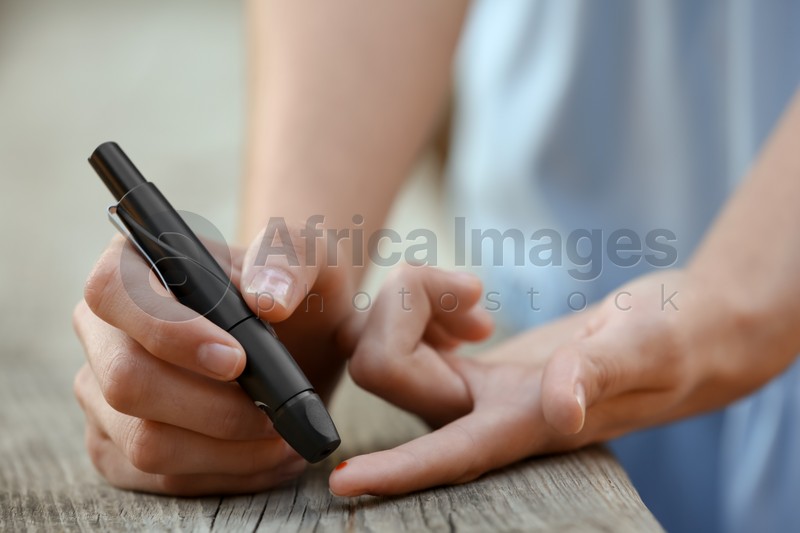 Woman using lancet pen near wooden surface outdoors. Diabetes control