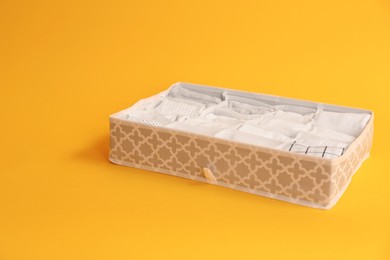Textile organizer with folded clothes on yellow background