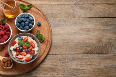 Tasty oatmeal porridge with berries and almond nuts served on wooden table, top view. Space for text