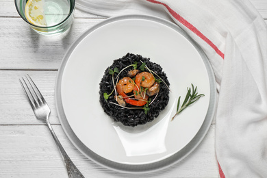 Delicious black risotto with seafood served on white wooden table, flat lay