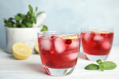 Tasty refreshing cranberry cocktail with lemon on white wooden table, closeup