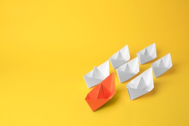 Photo of Group of paper boats following orange one on yellow background, space for text. Leadership concept