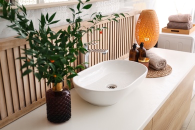 Vase with beautiful branches and candles near vessel sink in bathroom. Interior design